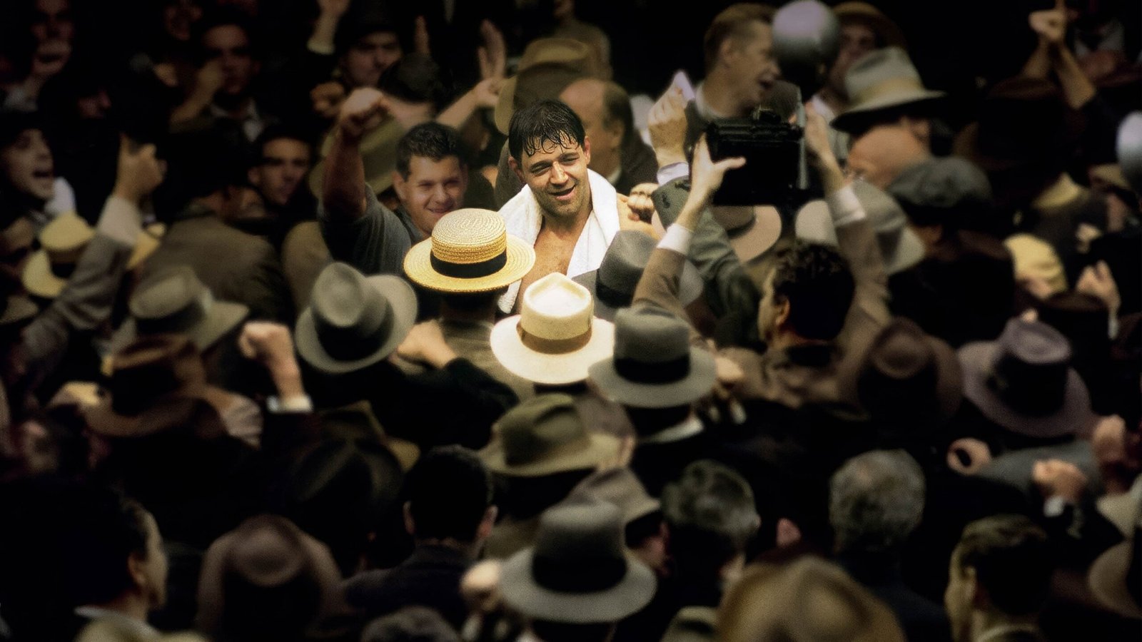Smiling man with a towel around his neck in a crowded party, surrounded by people wearing hats.